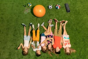 Group of happy children playing outdoors. Kids having fun in spring park. Friends lying on green grass. Top view portrait