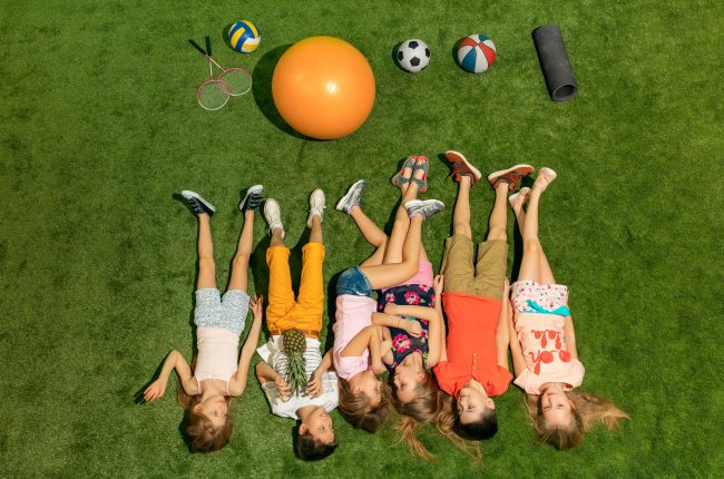 Group of happy children playing outdoors. Kids having fun in spring park. Friends lying on green grass. Top view portrait